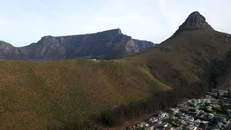 Cinematic-Pull-Away-Aerial-Shot-of-Lion's-Head-Peak-with-Table-Mountain-and-Signal-Hill-During-Golden-Hour-Sunset