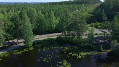 Seguimiento-De-Imágenes-De-Drones-Sobre-Un-Pequeño-Lago-Que-Muestra-A-Dos-Corredores-En-Un-Camino-De-Grava