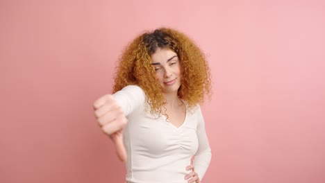woman expressing disapproval with thumbs down gesture on pink background
