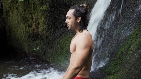 un joven en topless tomando un baño en un manantial y disfrutando del agua dulce de una hermosa cascada