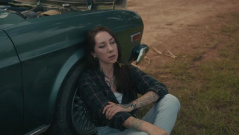 woman sitting beside broken-down vintage car