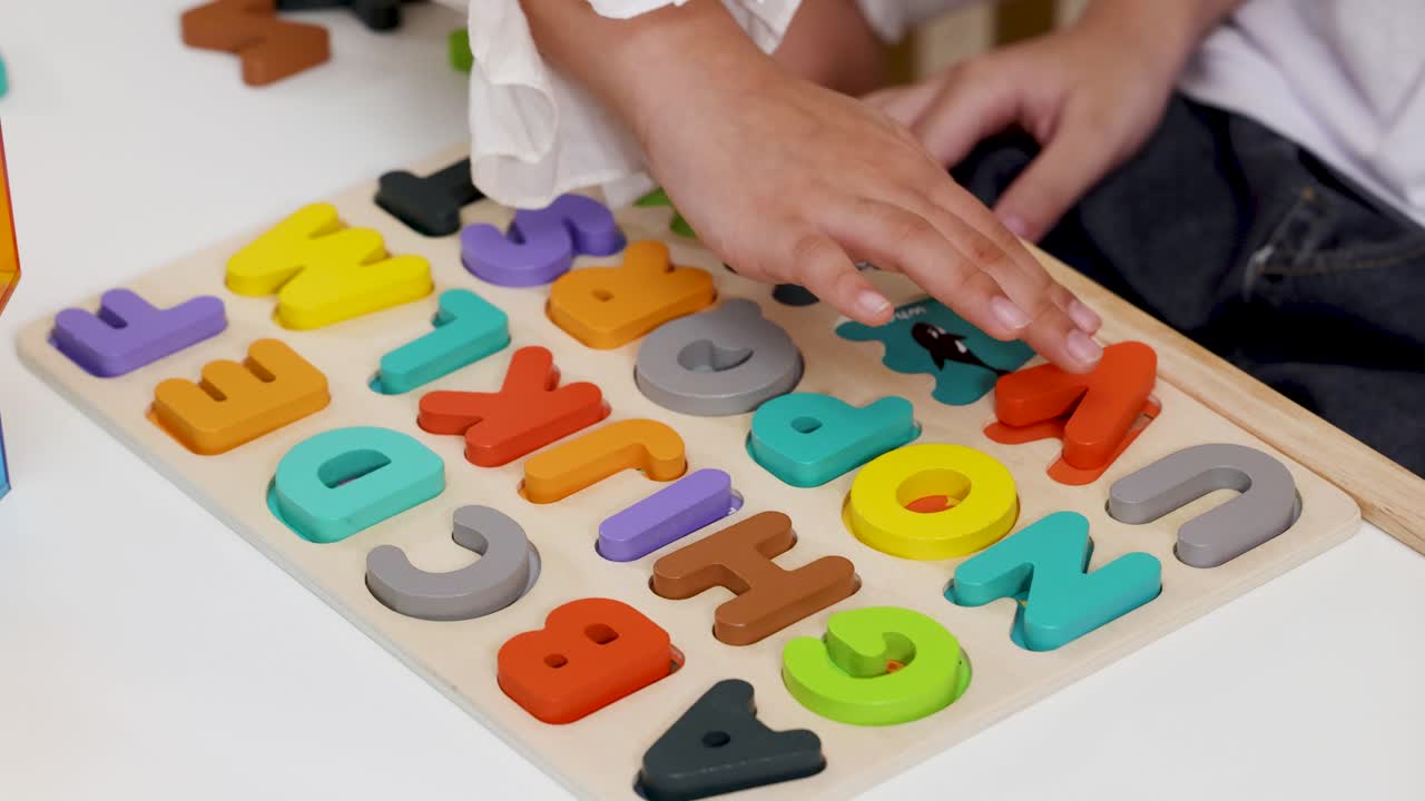 Kids fit wooden letters into puzzle board under bright natural light, viewed from overhead