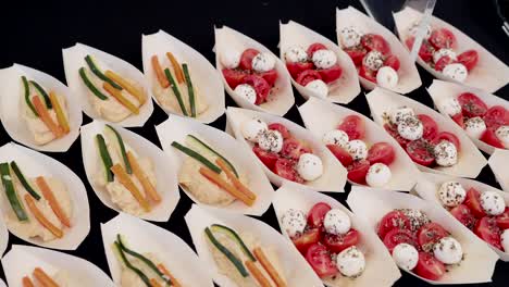 individual paper trays filled with hummus and veggie sticks next to caprese salad with herbs