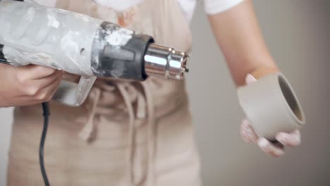 woman using a hot air tool to shape a clay pot