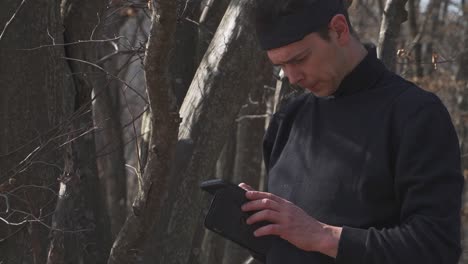a focused man dressed in black with a headband carefully examines a small pouch in a wooded area. perfect for themes of mystery, survival, or tactical preparation.