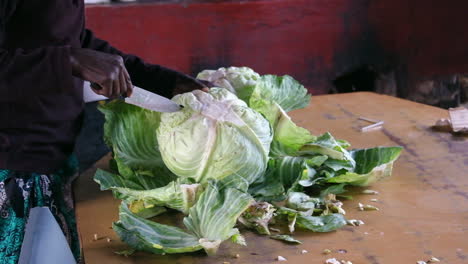 hands chopping large cabbage with a knife on a wooden table for meal preparation