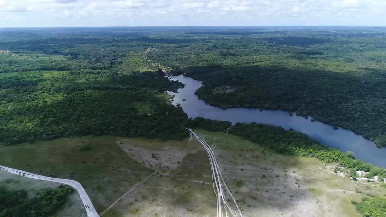 Riprese aeree con drone che si muove in avanti di un pittoresco fiume serpeggiante visto dall'alto, circondato da una lussureggiante foresta verde, di giorno a Parintins, Amazonas, Brasile.