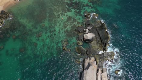 slow cinematic drone tilt down over beautiful rock in ocean with waves