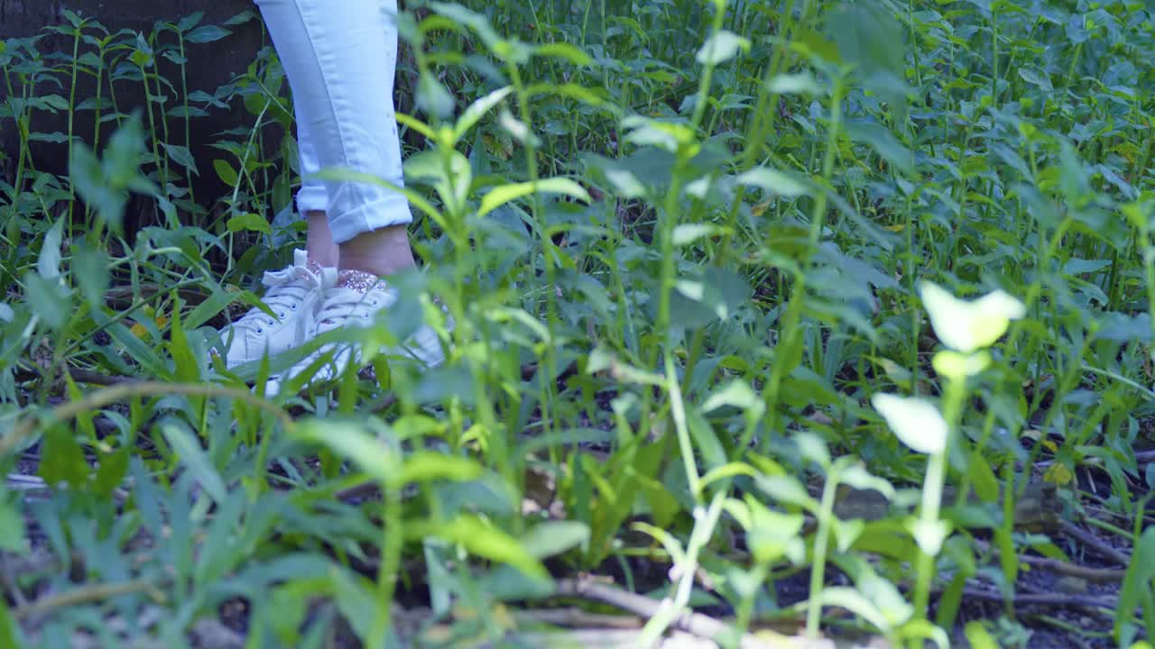 vista de cerca de los pies y zapatillas de una joven en un parque tropical con arbustos en primer plano