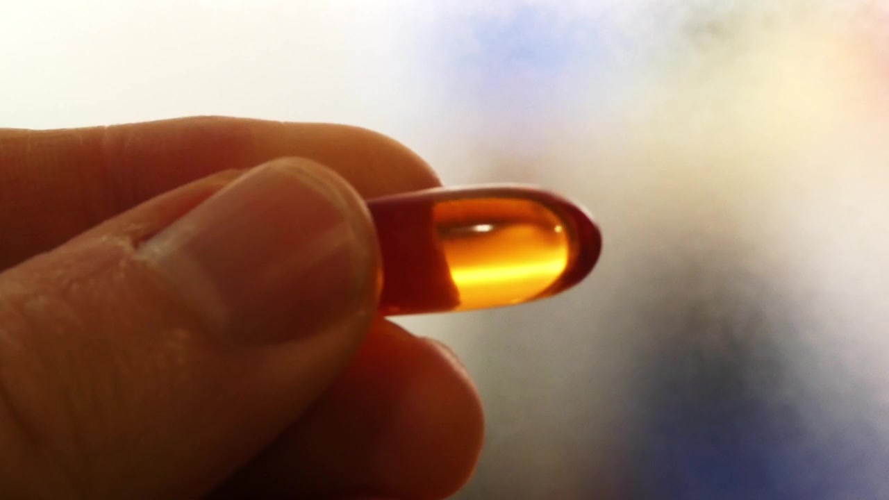 Primo piano di una mano che tiene una capsula molle trasparente di vitamina omega 3 olio di pesce in controluce.