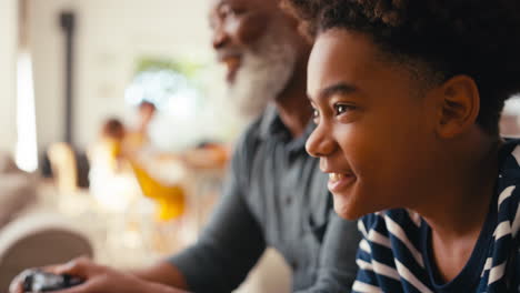 Close-Up-Of-Grandfather-And-Grandson-Sitting-On-Sofa-At-Home-Playing-Video-Game-Together