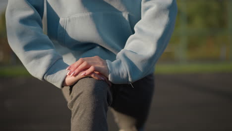 close up partial view of lady in blue sweater engaging in outdoor exercise with blurred background featuring greenery and bar fence, emphasizing fitness and stretching