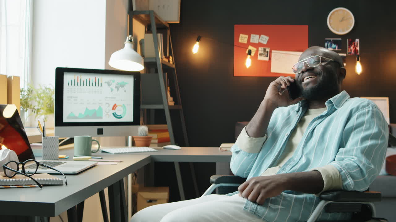 Uomo afroamericano in sedia a rotelle che parla al telefono nel suo ufficio domestico