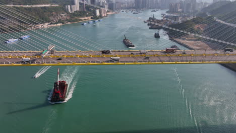 cargo barge sailing under the ting kau bridge while vehicles driving over the highway on a clear sunny morning