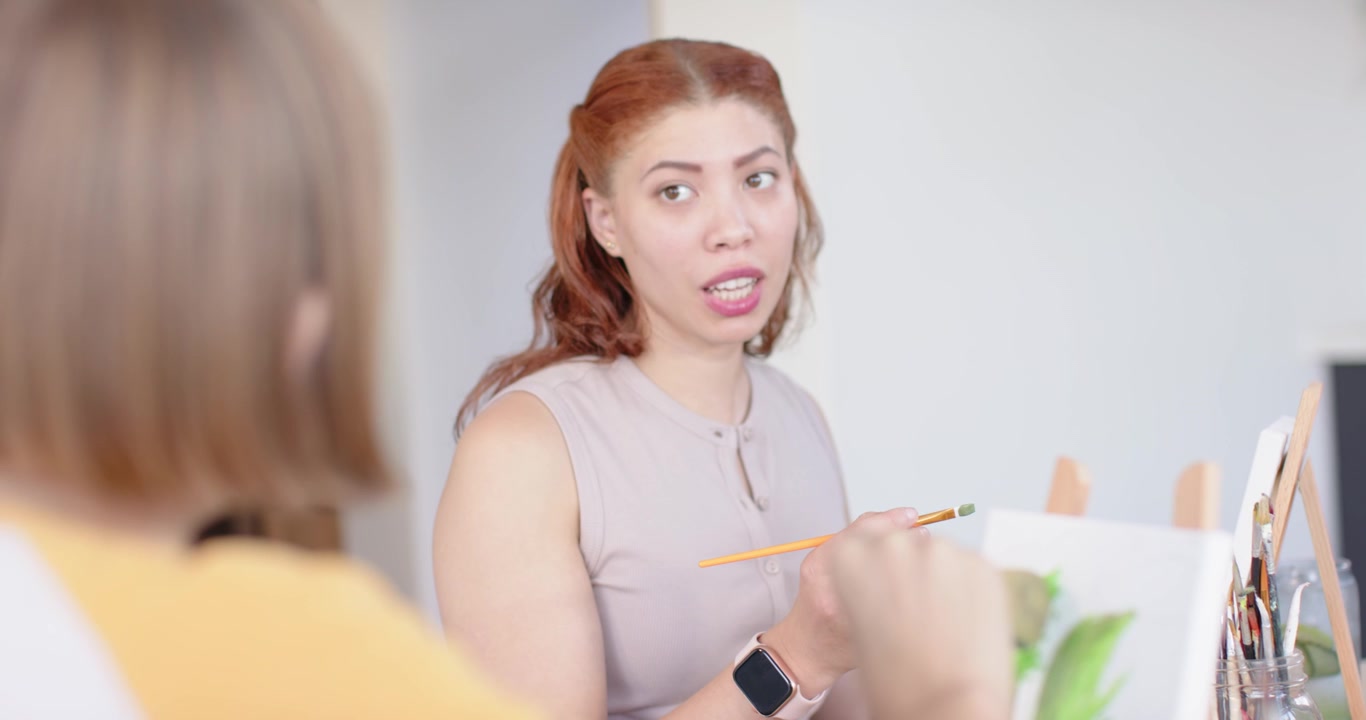 Female friends painting at studio, painter adding green strokes, redhead woman teaching brushwork