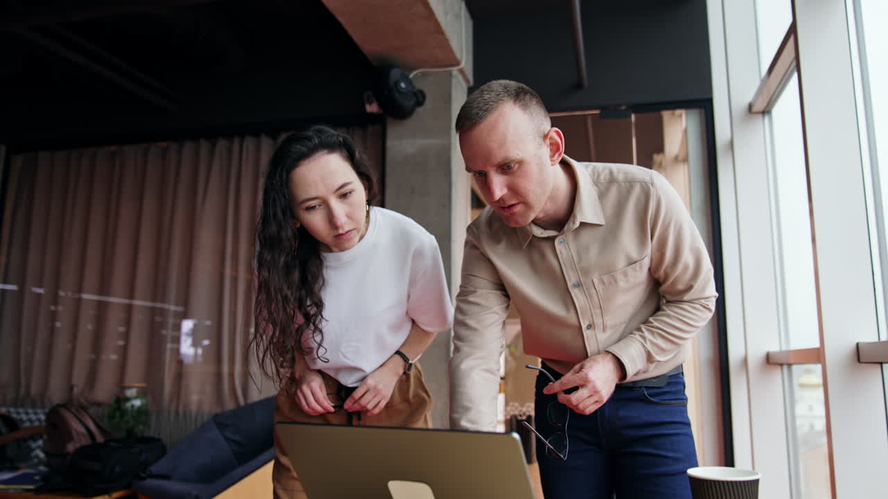 Pair of colleagues are puzzled by some problem on computer. Male and female look at laptop screen attentively trying to find the solution.