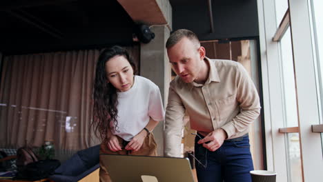 pair of colleagues are puzzled by some problem on computer. male and female look at laptop screen attentively trying to find the solution.