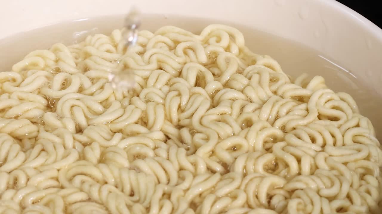 Un flusso costante di acqua bollente idrata i noodles ramen secchi in una ciotola bianca