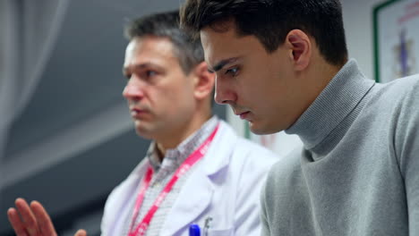 Young male student listens to the educator wearing white robe attentively. Neurosurgery training for future surgeons.