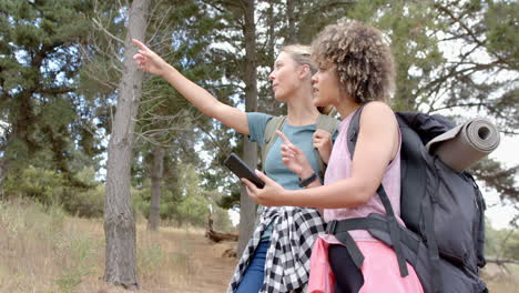 a young caucasian woman points out something in the distance while hiking with a young biracial woma