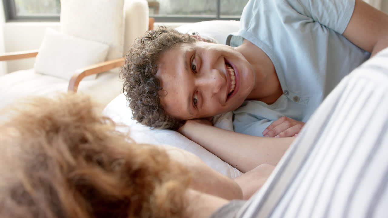 Felice coppia gay maschile multietnica sdraiata sul letto che parla a casa, al rallentatore