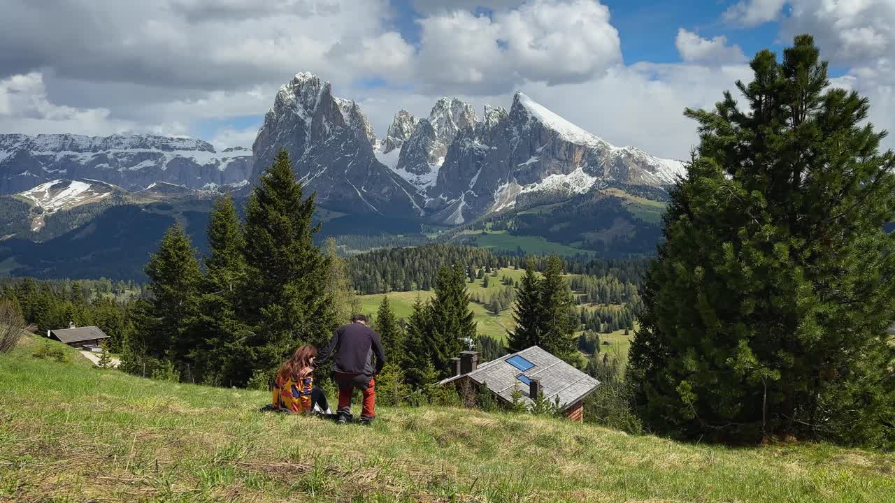 Scenic footage of a couple socializing in the Alpi di Siusi, surrounded by meadows and Dolomite mountains under a cloudy sky