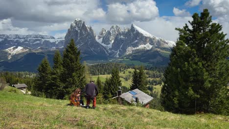 scenic footage of a couple socializing in the alpi di siusi, surrounded by meadows and dolomite mountains under a cloudy sky