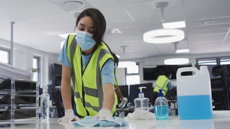 Mujer-Con-Chaleco-De-Alta-Visibilidad-Y-Mascarilla-Limpiando-La-Oficina-Con-Desinfectante