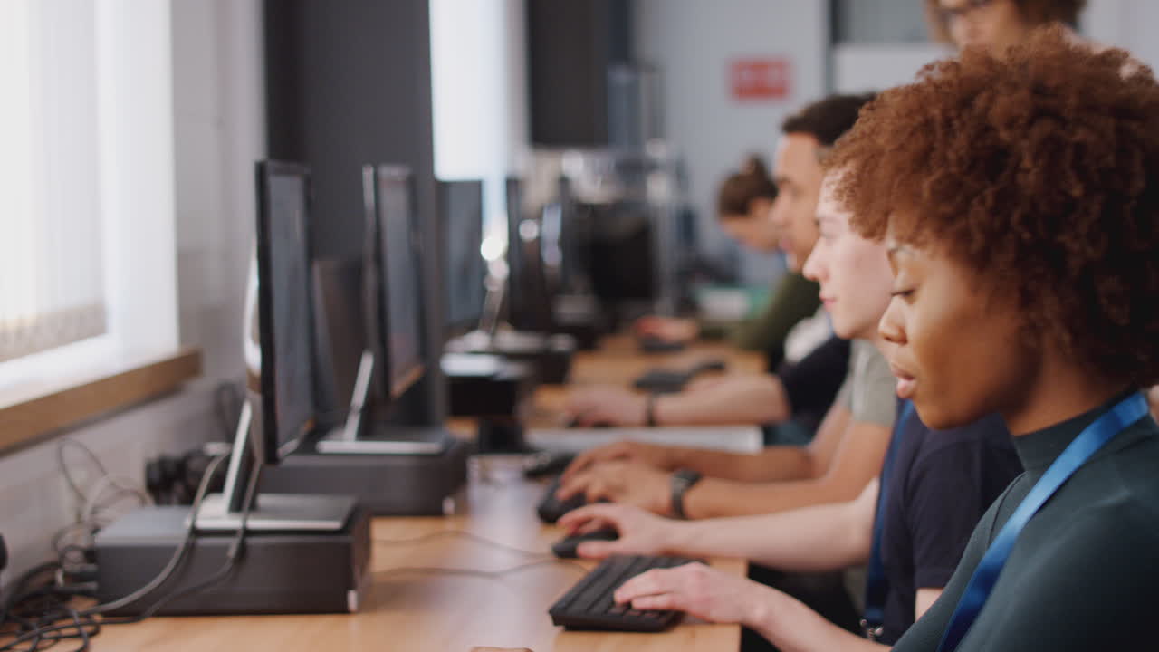 Group Of College Students With Tutor Studying Computer Design Sitting At Monitors In Classroom