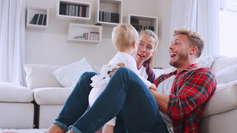 Una-Pareja-Joven-Sentada-En-El-Suelo-Jugando-Con-Su-Hija-En-Casa