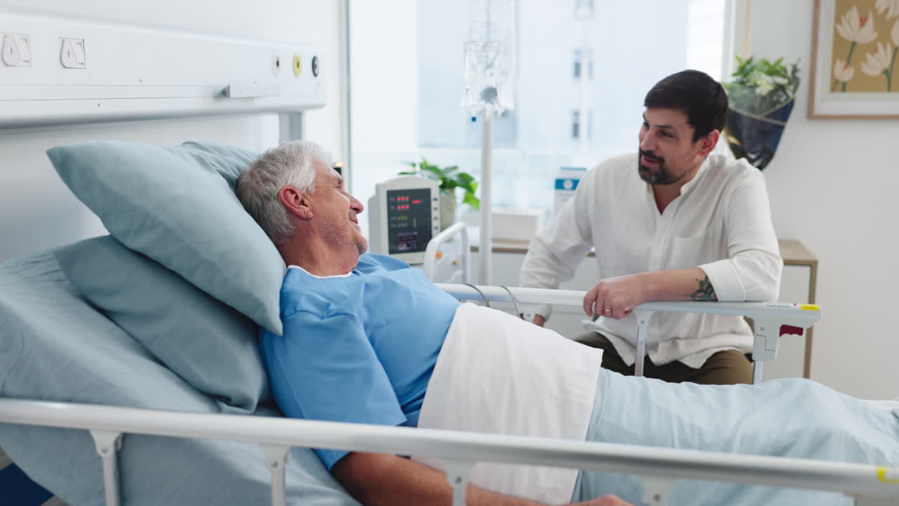 Giovane uomo visita il padre anziano nel letto d'ospedale per conversare.
