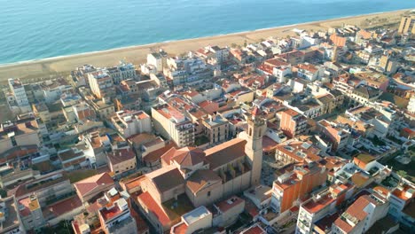 aerial view highlighting the historic calella de mar cathedral, surrounded by vibrant town structures and coastline. captures the charm of spain's coastal architecture