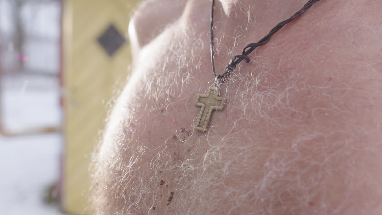 Christian cross necklace on bare chested man in snow flurry looking up, pedestal