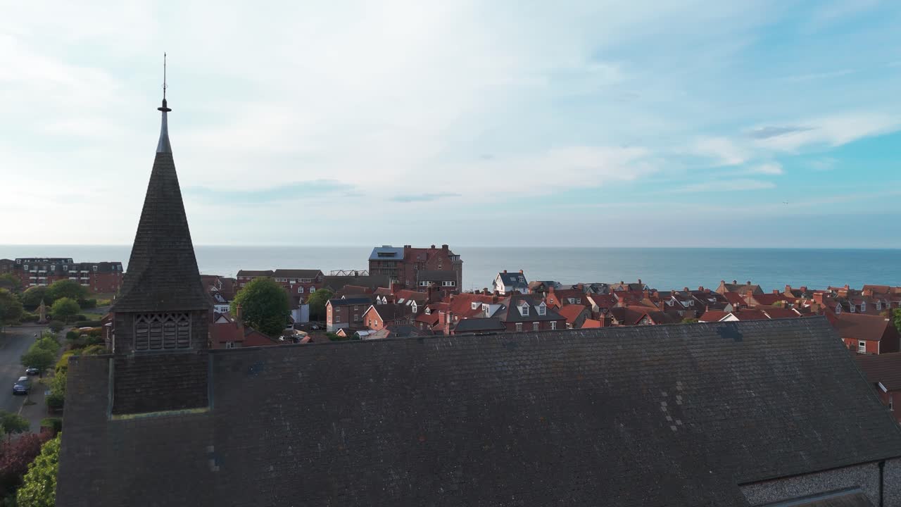 View of Sheringham rooftops with St Peter’s Church steeple and calm blue sea behind