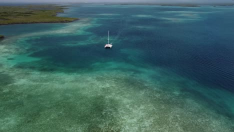 Toma-Aérea-De-Un-Catamarán-O-Bote-En-Medio-De-Una-Zona-De-Playa-Con-Aguas-Cristalinas-Y-Corales,-En-Tucacas,-Venezuela