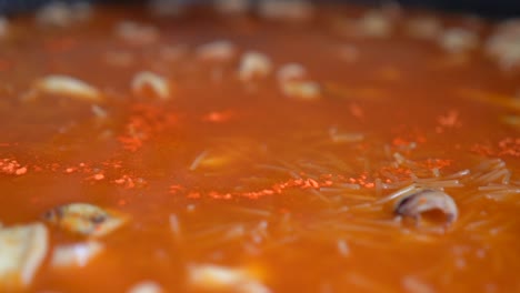 echando azafrán al caldo para fideuá en paellón con arreglo de pescado