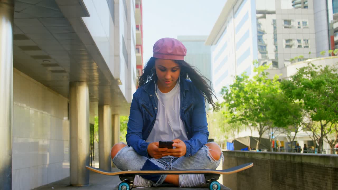 Female dancer with skateboard using mobile phone in the city 4k