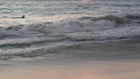 Tilt-reveal-of-surfer-paddling-in-the-ocean-and-a-picturesque-sunset-in-the-background