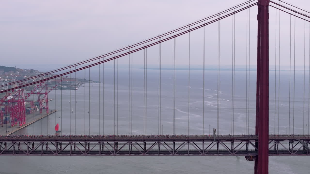 Side-on aerial drone shot of half marathon and 10K long-distance running event in Lisbon, Portugal, Europe. Runners crossing the iconic famous red 25th April suspension bridge. Drone flying backwards