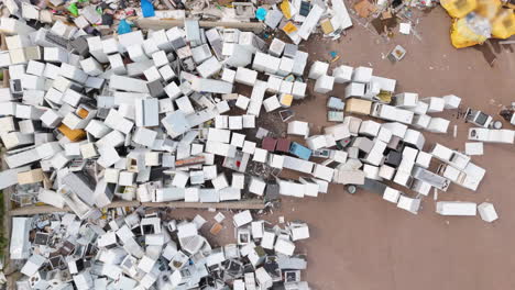 white discarded appliances thrown haphazardly onto scrapyard pile, aerial riser