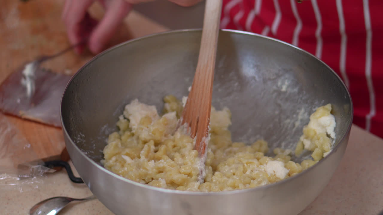 Woman Mixing Bryndza Cheese To Coat The Hot Halusky Dumplings On The Bowl. - close up