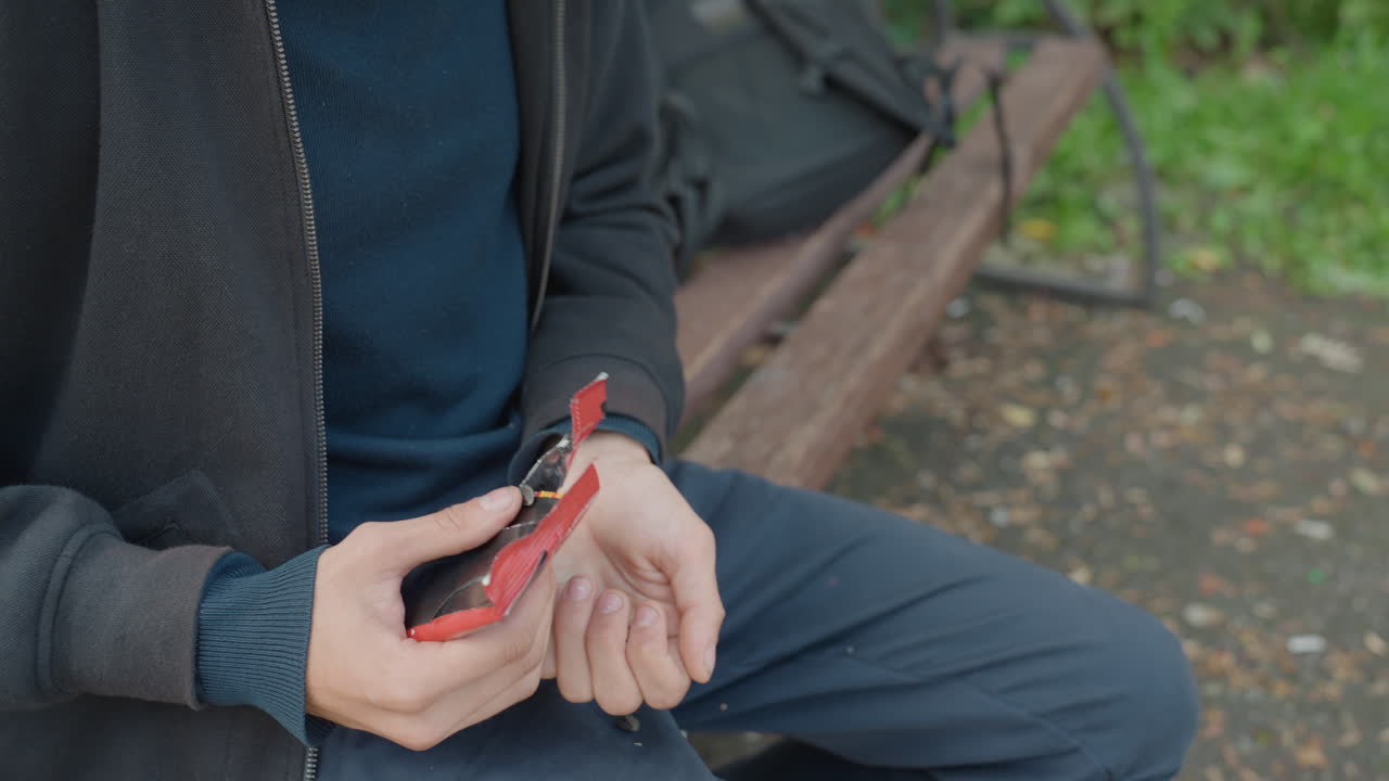 ベンチに座って手のひらに乗せた種で赤い鳥に餌をやる男性、手と鳥のクローズアップ、カジュアルなジャケット、紺色のパンツ、公園の小道と緑の草の背景、穏やかな動き、穏やかな秋の雰囲気、親密な瞬間