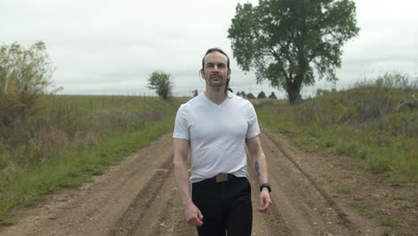 man walking on dirt road by expansive fields