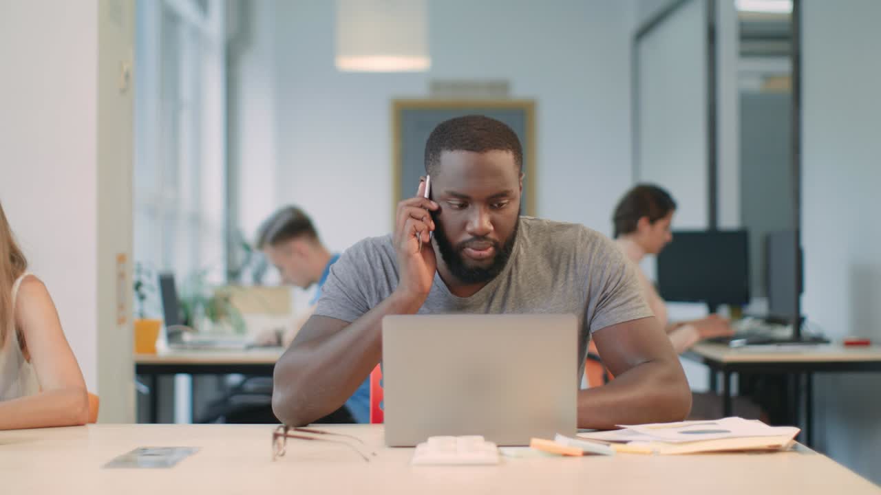 Forretningsmand arbejder på bærbar computer i et coworking-område. Freelancer taler i mobiltelefon
