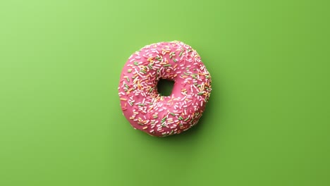 donut dulce con glaseado rosado encima de pastel aislado en verde. filmado en cámara de cine 4k red raven