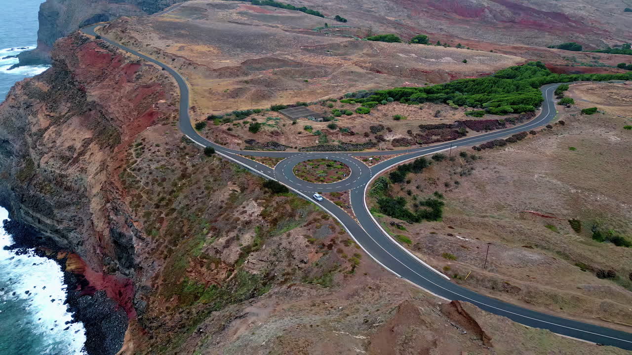 Rotatoria aerea su costa rocciosa con acqua oceanica tempestosa. Auto che percorre la strada