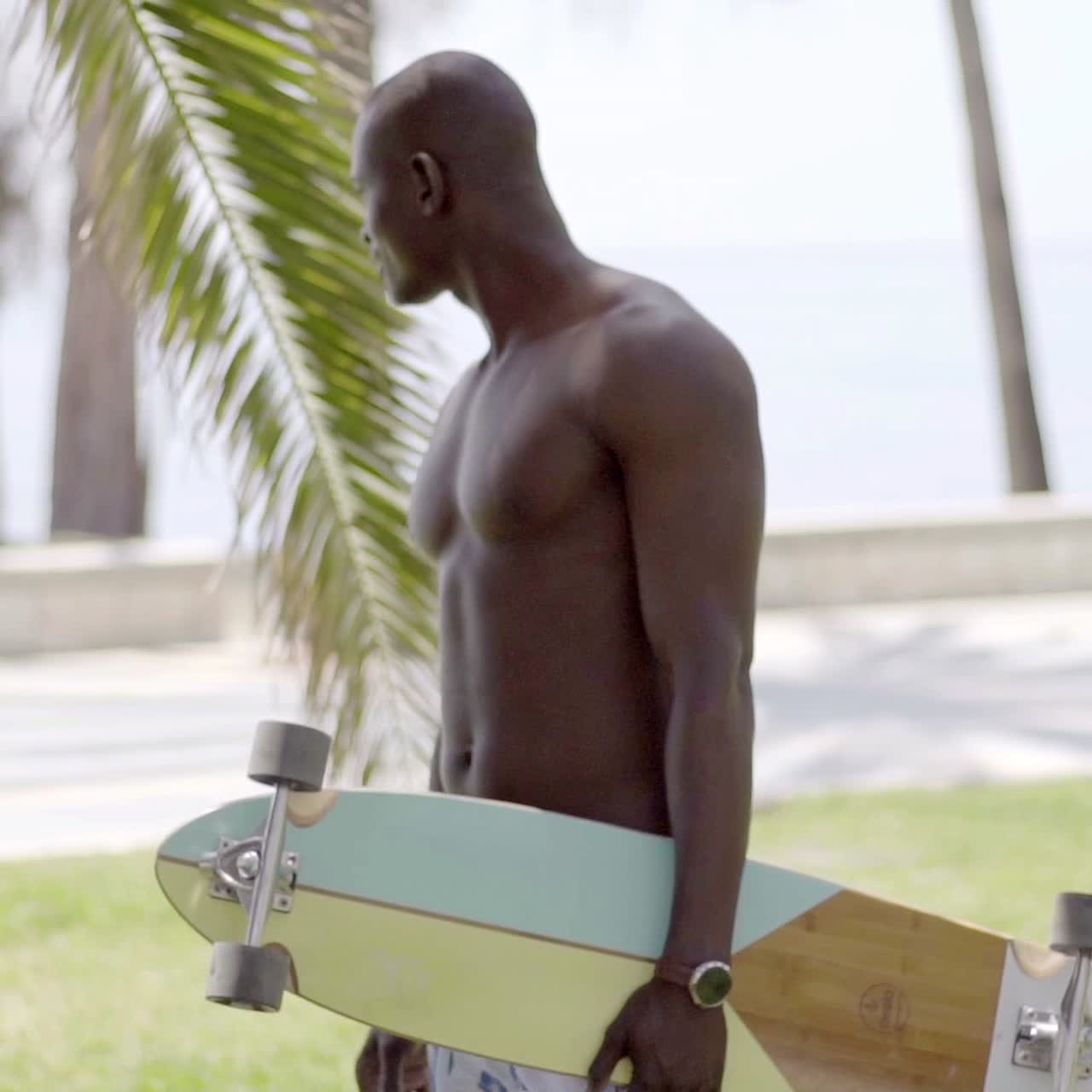 Skater nero a torso nudo che cammina in un parco erboso