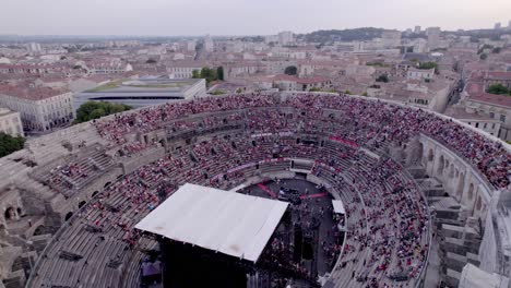 Drone-Sobre-La-Arena-De-Nimes-Al-Atardecer,-La-Gente-Está-Esperando-El-Concierto-De-Stromae