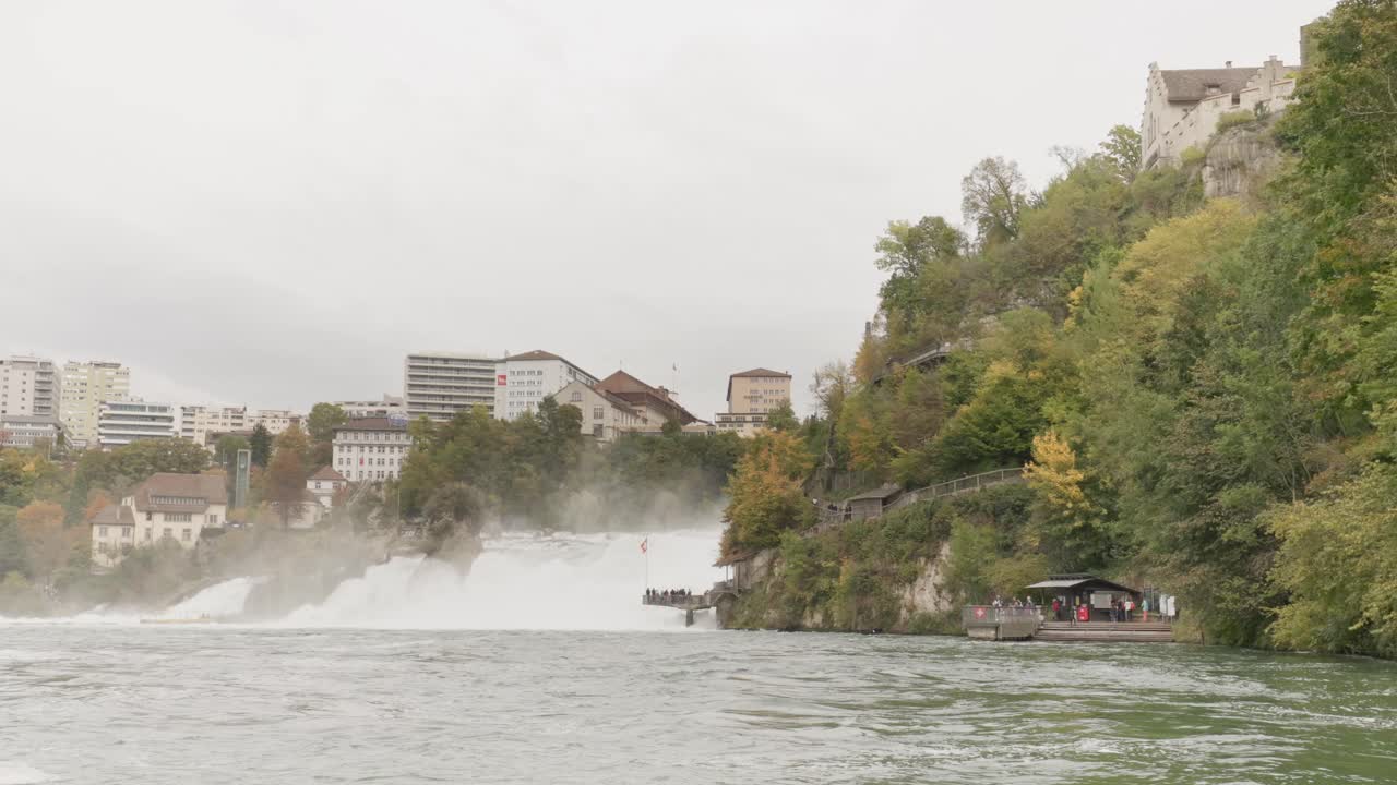 A dramatic footage of Rheinfall, captured on a cloudy day as the camera moves closer to the powerful waterfall. The mist and overcast sky enhance the scene's intensity.