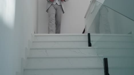 elegant groom in a light gray suit walking down white marble stairs before the ceremony